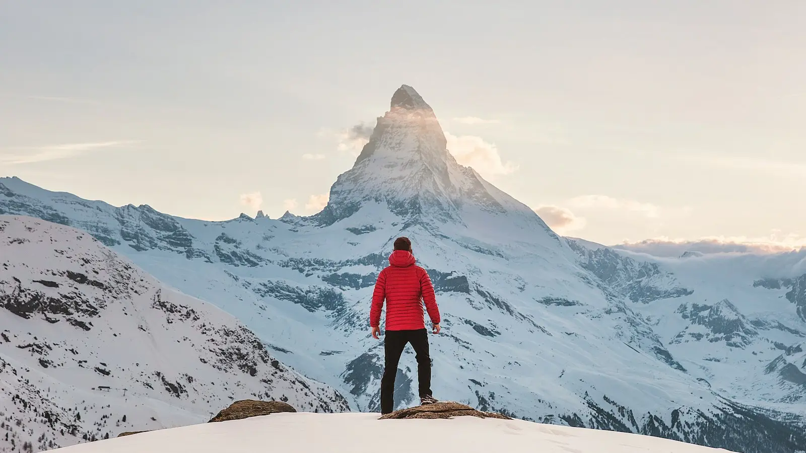 Person in red hoodie standing on snowy mountain during daytime