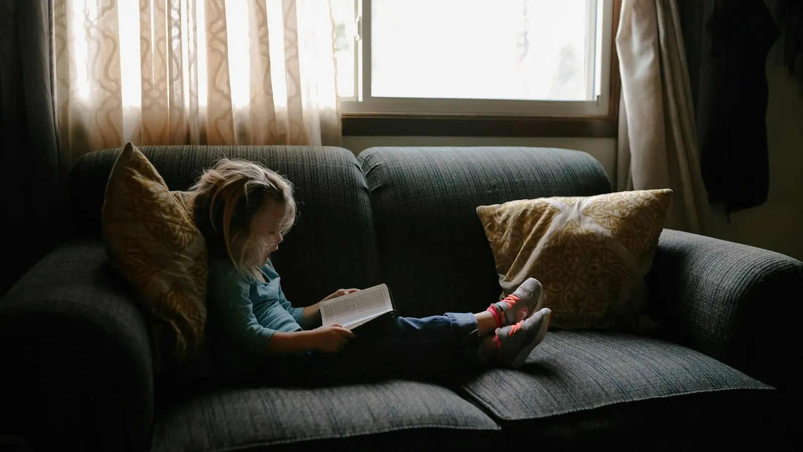 Girl reading book sitting on sofa